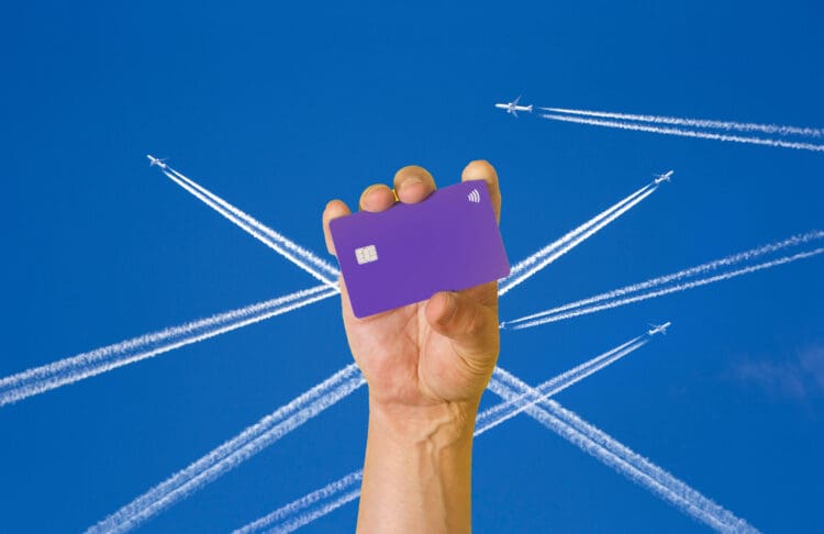 A hand holds up what could be a Delta Amex Reserve Card. Art of airliner contrails are in the background.