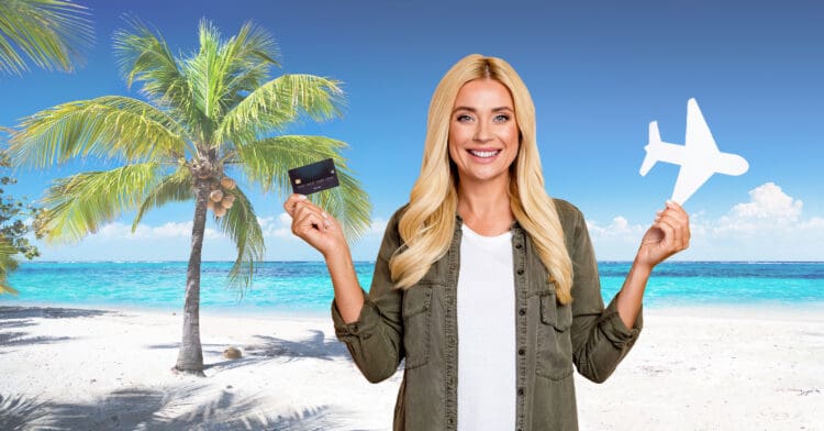 A woman poses with a credit card and airplane cutout on a tropical beach