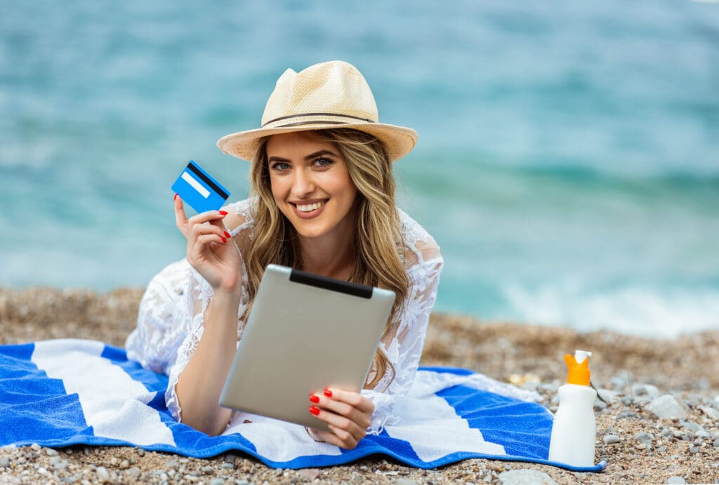 a woman lying on a towel holding a tablet and a credit card