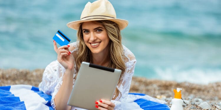 a woman lying on a towel holding a tablet and a credit card