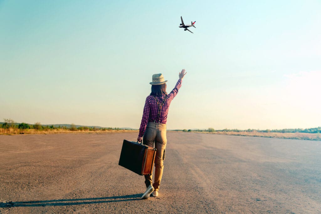 Traveler woman with vintage suitcase waves to a departing Delta Air Lines plane.