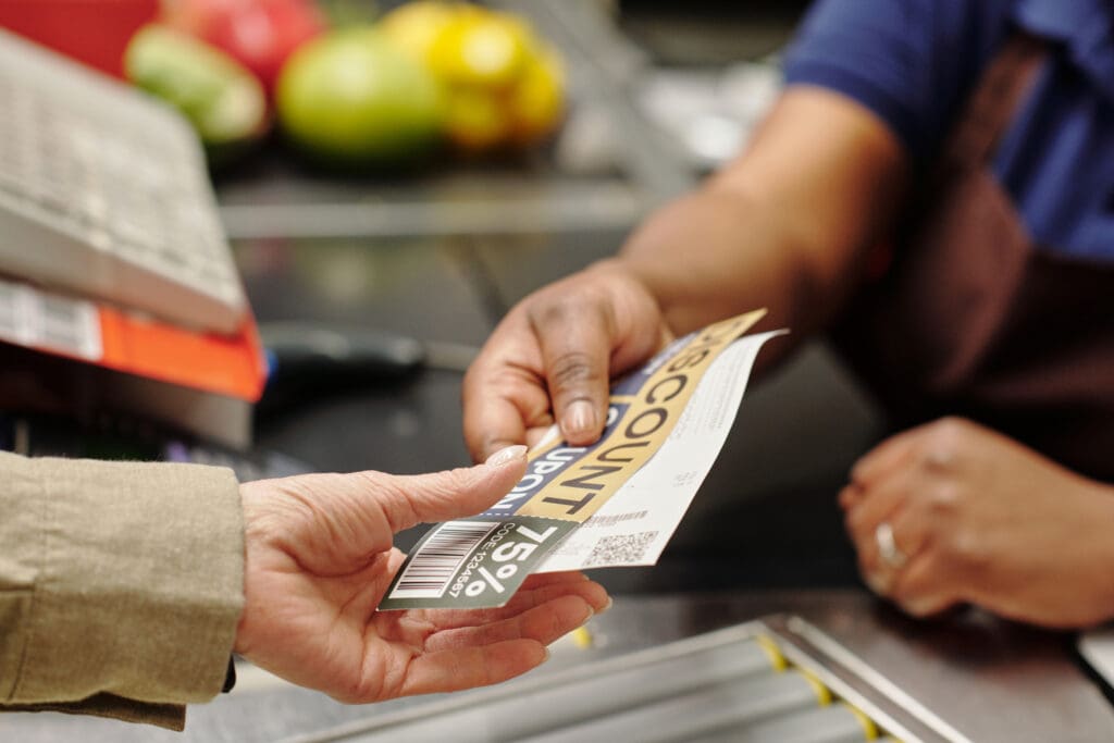  cashier passing discount coupon and receipt to customer over checkout counter in supermarket