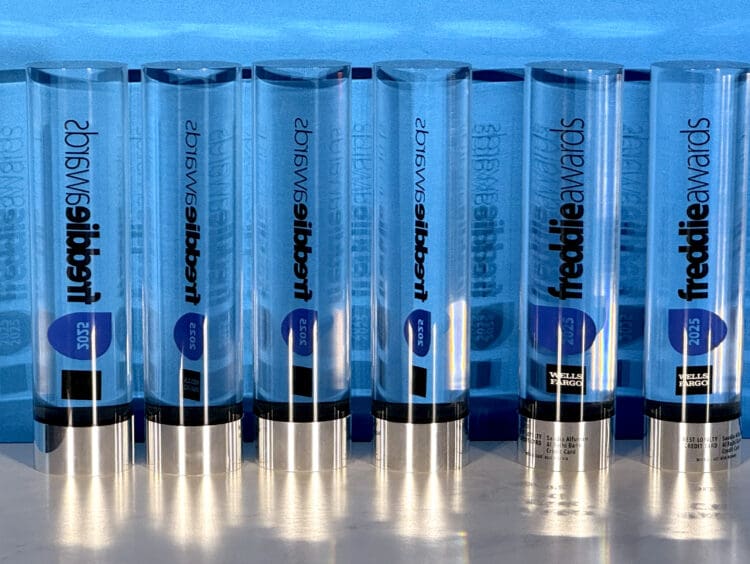 The image shows a row of transparent, cylindrical awards with blue accents. The awards are labeled "freddie awards" and have the year "2025" on them. They are standing upright on a reflective surface, and the name "Wells Fargo" is visible on some of the awards.