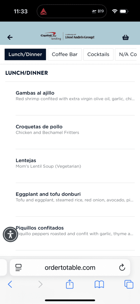 The image shows a digital menu from a website, featuring a "Lunch/Dinner" section. It includes the following dishes: 1. Gambas al ajillo - Red shrimp confited with extra virgin olive oil, garlic, and chili. 2. Croquetas de pollo - Chicken and Bechamel Fritters. 3. Lentejas - Mom’s Lentil Soup (Vegetarian). 4. Eggplant and tofu donburi - Tofu and eggplant, steamed rice, red onion, avocado, and pickles. 5. Piquillos confitados - Piquillo peppers roasted and confit with garlic, thyme, and olive oil. The menu is part of a collaboration with José Andrés Group and is associated with Capital One Landing. The website URL at the bottom is "ordertotable.com".