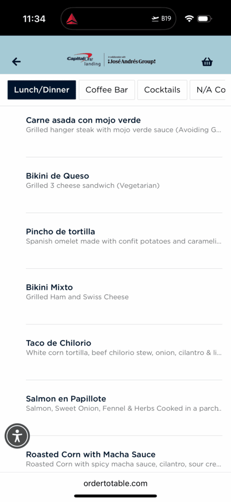 The image shows a digital menu for lunch and dinner options. It includes: 1. **Carne asada con mojo verde** - Grilled hanger steak with mojo verde sauce. 2. **Bikini de Queso** - Grilled 3 cheese sandwich (Vegetarian). 3. **Pincho de tortilla** - Spanish omelet with confit potatoes and caramelized onions. 4. **Bikini Mixto** - Grilled ham and Swiss cheese. 5. **Taco de Chilorio** - White corn tortilla with beef chilorio stew, onion, cilantro, and lime. 6. **Salmon en Papillote** - Salmon with sweet onion, fennel, and herbs cooked in parchment. 7. **Roasted Corn with Macha Sauce** - Roasted corn with spicy macha sauce, cilantro, and sour cream. The menu is part of a collaboration with Capital One and José Andrés Group.