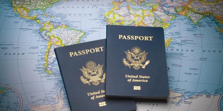 Two United States passports are placed on a world map. The passports are dark blue with the U.S. emblem and the words "United States of America" and "Passport" in gold lettering. The map underneath shows parts of North and South America, the Atlantic Ocean, and parts of Europe and Africa.