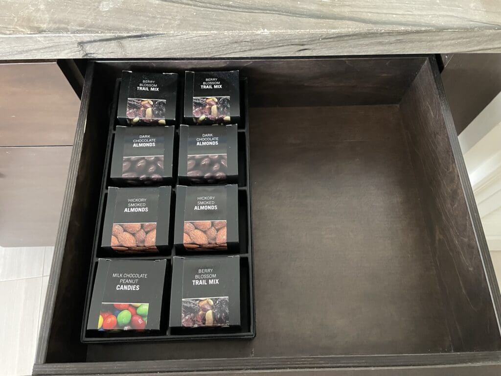 The image shows an open drawer containing neatly arranged snack boxes. There are two boxes of "Berry Blossom Trail Mix," two boxes of "Dark Chocolate Almonds," two boxes of "Hickory Smoked Almonds," and one box of "Milk Chocolate Peanut Candies." The right side of the drawer is empty.