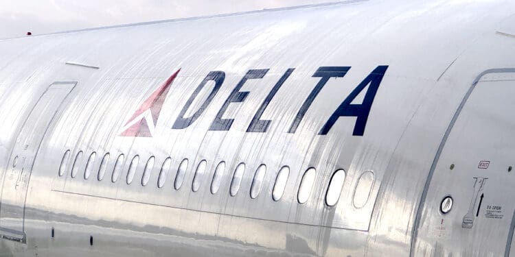 The image shows a close-up of the side of a Delta Air Lines airplane. The aircraft's metallic body is visible, with the Delta logo and name prominently displayed. There are several windows along the side, and the sky is overcast in the background. A Delta Air Lines A330-300 (©Eye of the Flyer)