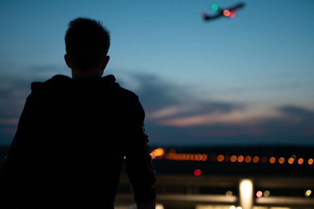 Man sits at the airport at night and watches a plane taking off