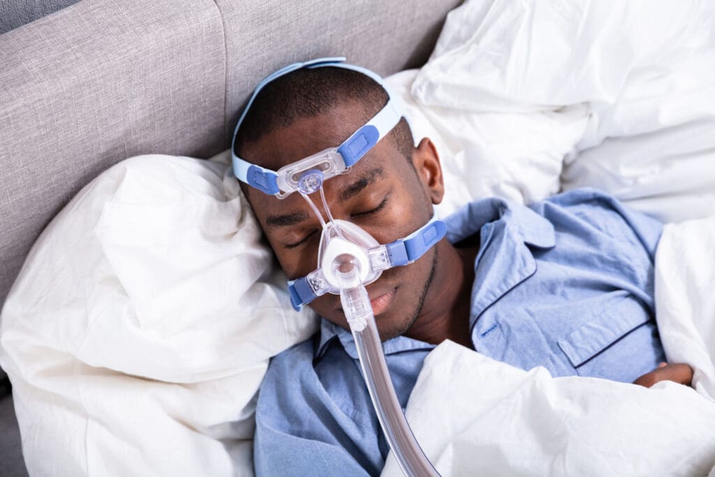 High Angle View Of A Man Wearing CPAP Mask Sleeping On Bed