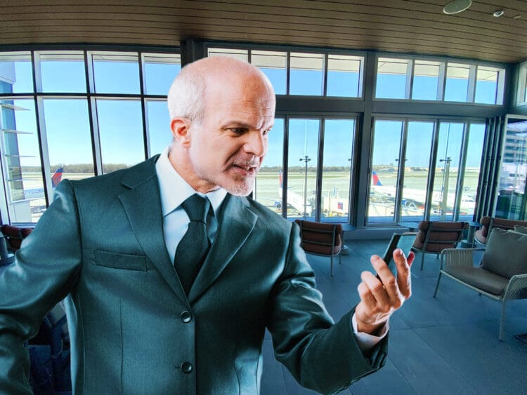 A business man takes a speakerphone call in an airport lounge.