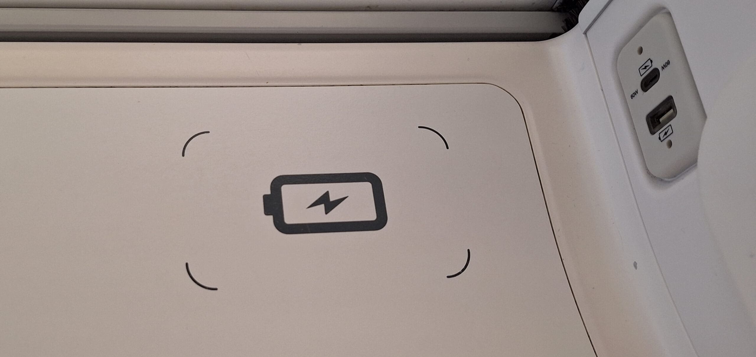 The image shows a wireless charging pad on a surface, indicated by a battery icon with a lightning bolt. To the right, there are two charging ports, one USB-C labeled "60W" and one USB-A, both with lightning bolt symbols.