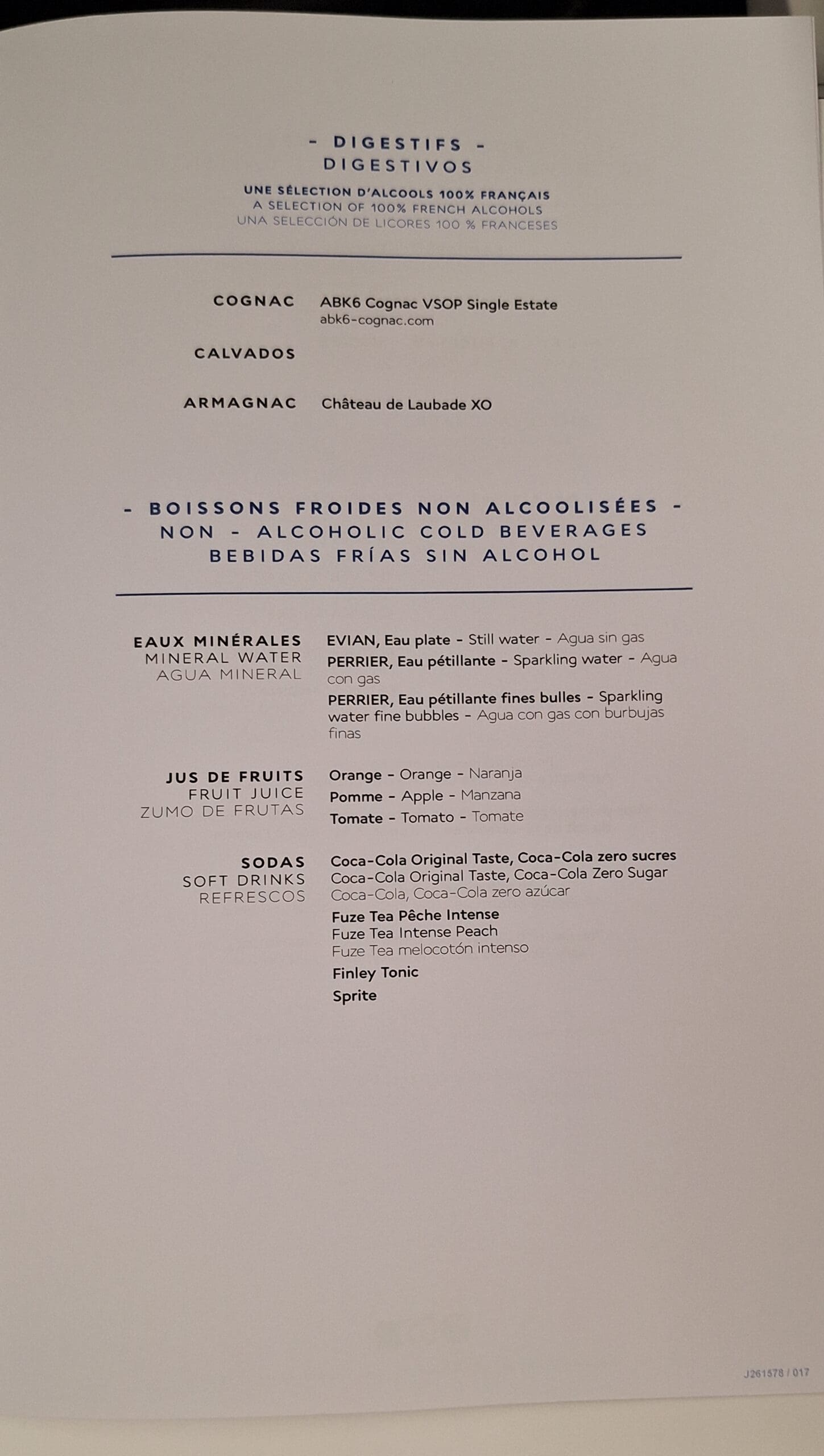 This image shows a menu listing digestifs and non-alcoholic cold beverages. The digestifs section includes options like ABK6 Cognac VSOP Single Estate, Calvados, and Château de Laubade XO Armagnac. The non-alcoholic beverages section lists mineral waters such as Evian and Perrier, fruit juices like orange, apple, and tomato, and sodas including Coca-Cola, Fuze Tea, Finley Tonic, and Sprite. The text is presented in French, English, and Spanish.