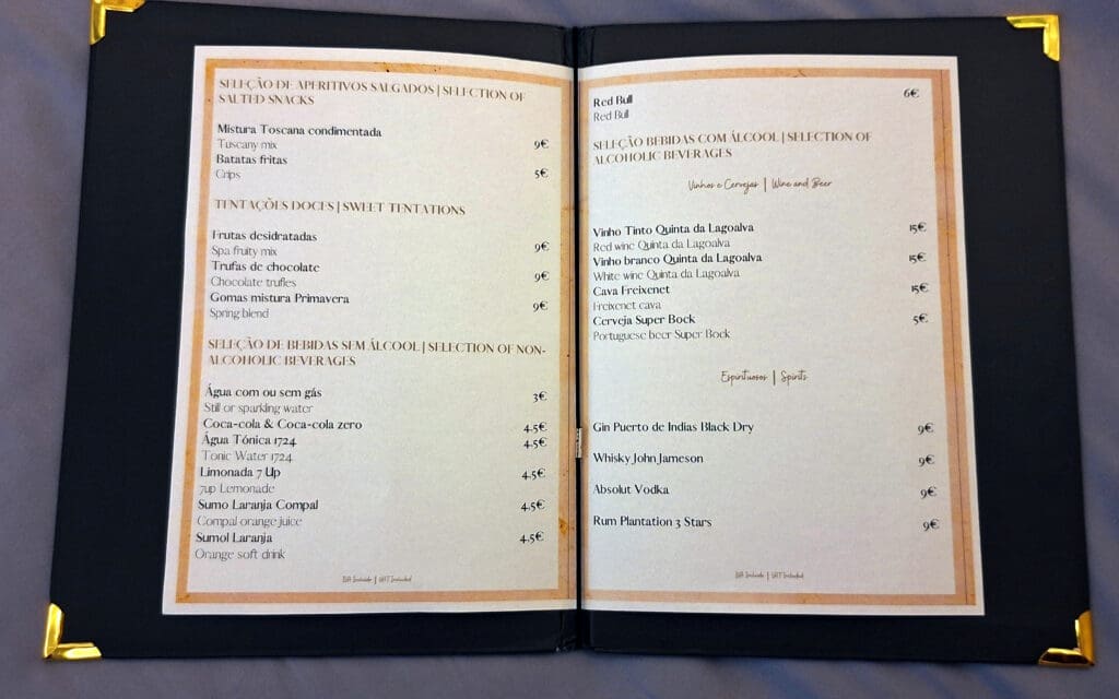 This image shows a menu with two pages. The left page lists salted snacks, sweet temptations, and non-alcoholic beverages, with items like "Tuscany mix," "Chocolate truffles," and "Coca-cola." Prices are in euros. The right page features alcoholic beverages, including wines, beer, and spirits, such as "Red wine Quinta da Lagoalva," "Super Bock beer," and "Gin Puerto de Indias Black Dry." Prices are also in euros. The menu is presented in both Portuguese and English.