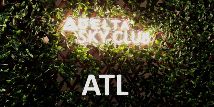 The image shows a wall covered with green leaves, featuring illuminated text that reads "DELTA SKY CLUB" at the top and "ATL" in larger letters below.