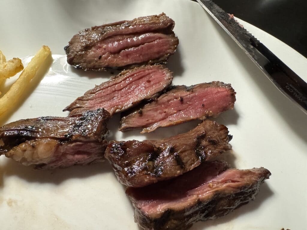 Steak frites at BLVD Steak in Calabasas, California. (©EyeOfTheFlyer.com) The image shows several slices of medium-rare steak on a white plate. The steak is cooked with a pink center and a seared exterior. There is a knife on the plate and a few French fries on the side.