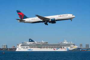 A Delta Air Lines 767 flies over an NCL cruise ship in a harbor
