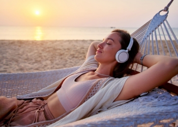 Young blissful calm woman wearing wireless headphones with closed eyes and hands behind head lie in a hammock and enjoy relaxing music