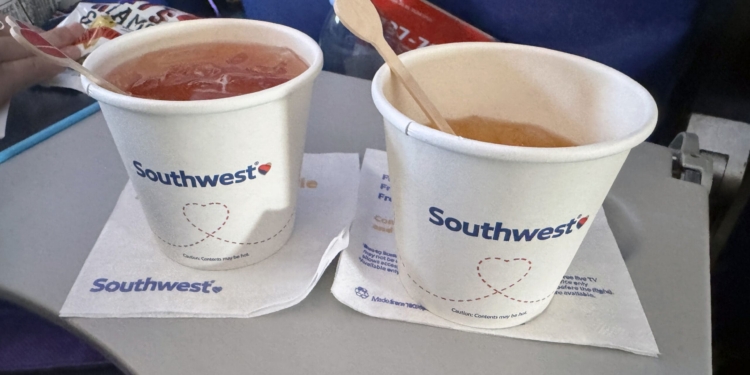 Two Southwest Airlines paper cups holding iced beverages with wooden stir sticks, sitting on Southwest napkins on a tray table