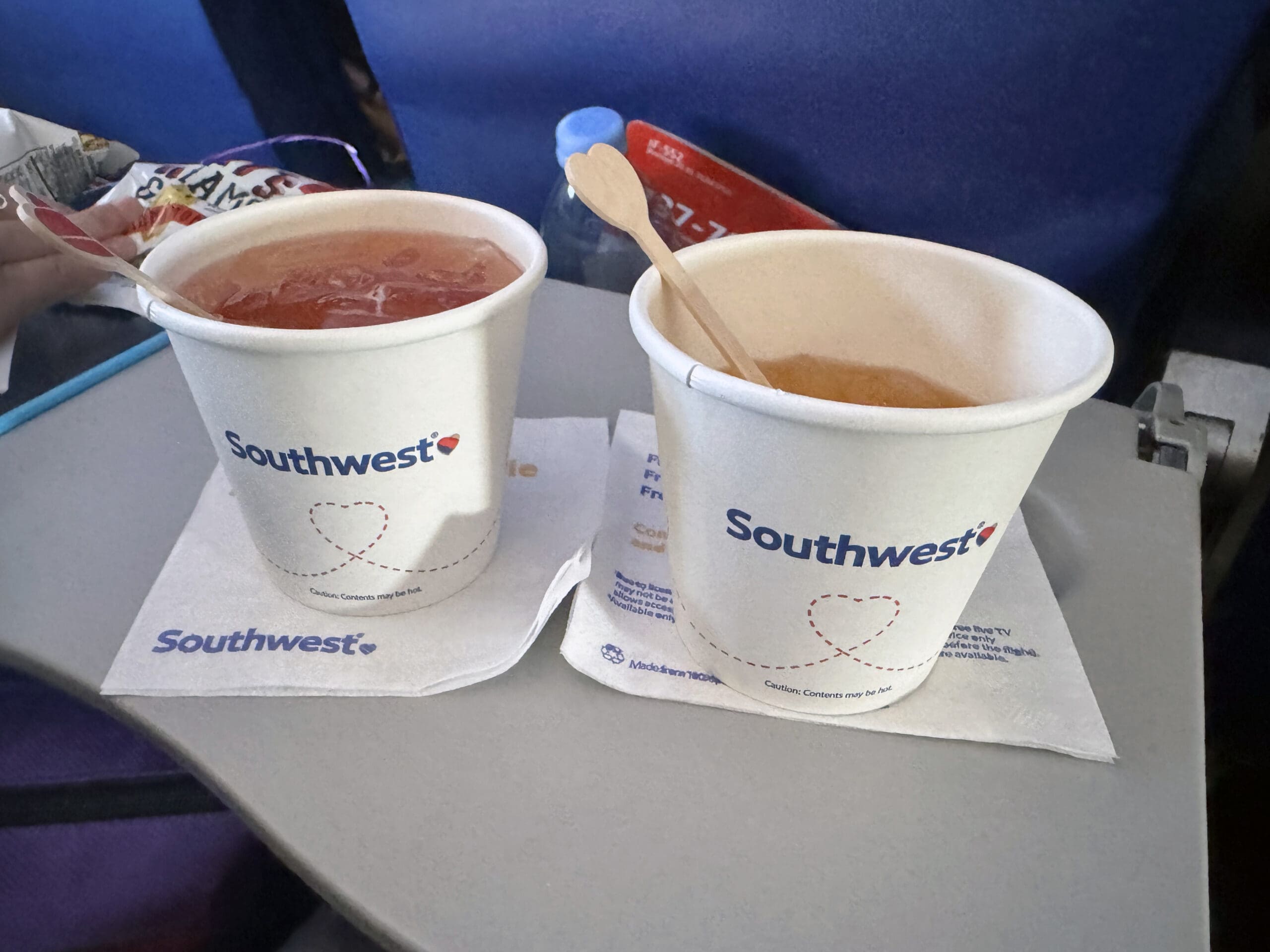 Two Southwest Airlines paper cups holding iced beverages with wooden stir sticks, sitting on Southwest napkins on a tray table