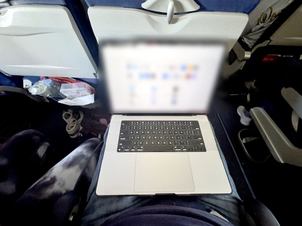 Open 16-inch MacBook Pro resting comfortably on a lap in a Southwest Extra Legroom seat with the seatback well ahead