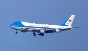 A clear, iconic view of Air Force One, the distinctive blue and white Boeing VC-25, majestically soaring through a bright, cloudless sky.