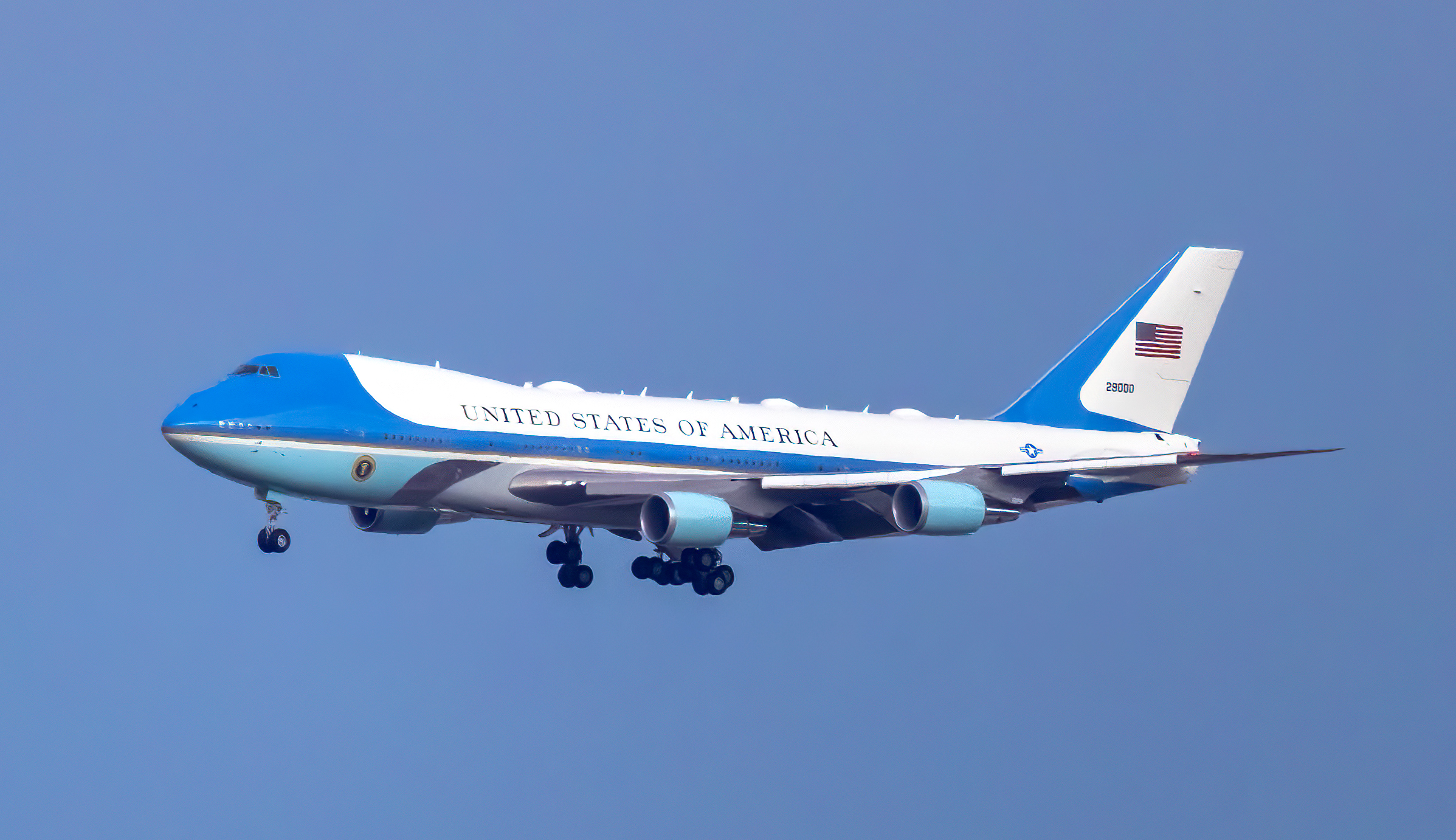 A clear, iconic view of Air Force One, the distinctive blue and white Boeing VC-25, majestically soaring through a bright, cloudless sky.
