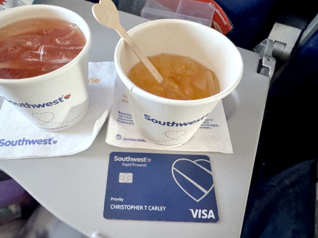 Two Southwest inflight drinks on a tray table beside a Southwest Rapid Rewards Priority Visa credit card